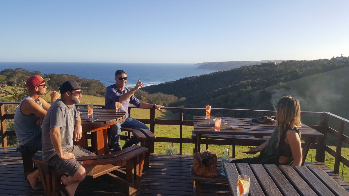 Guests sitting at the wooden tables on the Wildfarm deck with drinks, looking out over the hills and the ocean